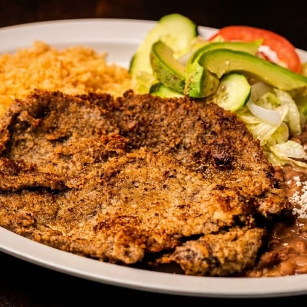 Breaded steak with rice, refried beans topped with cheese, and a side salad with avocado.