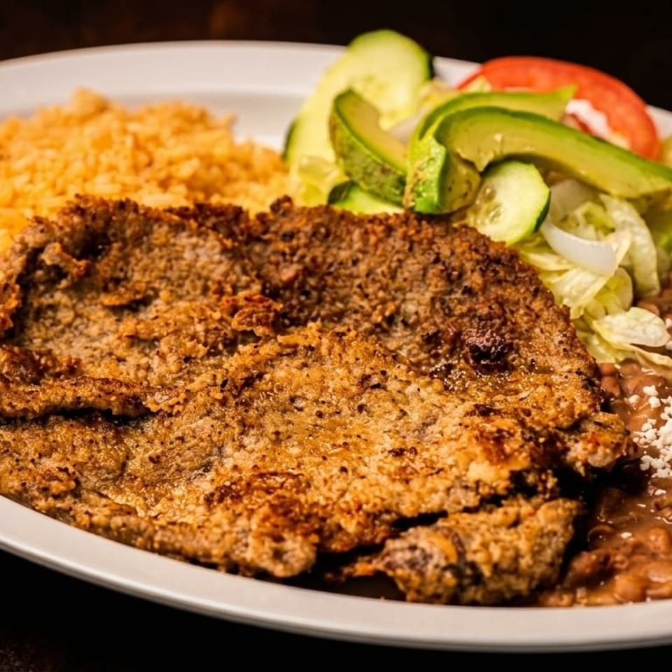 Breaded steak with rice, refried beans topped with cheese, and a side salad with avocado.