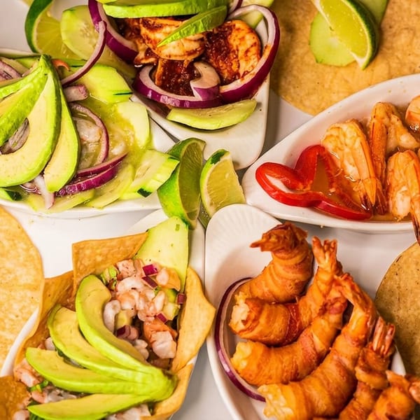A platter of various shrimp dishes, including ceviche, bacon-wrapped shrimp, and shrimp with peppers.