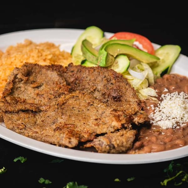 Breaded steak, orange rice, refried beans with cheese, and a fresh salad on a white plate.