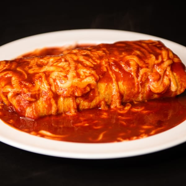 Steaming wet burrito or enchilada covered in rich red sauce and melted cheese on a white plate.