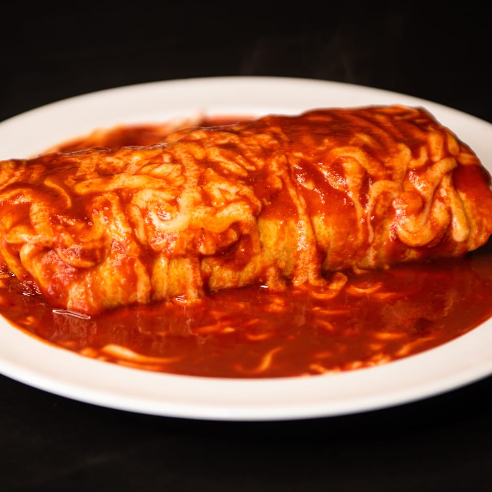 Large rolled pasta dish covered in melted cheese and tomato sauce, served on a white plate.