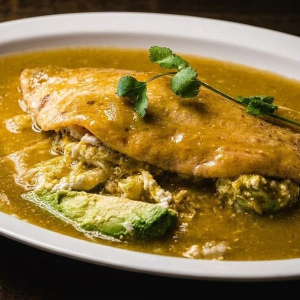 A Mexican dish with a golden omelet, scrambled eggs, and avocado in green salsa.