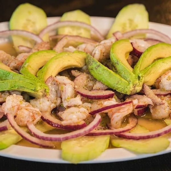 Shrimp ceviche with avocado, red onion, cucumber, and red bell pepper on a white plate.
