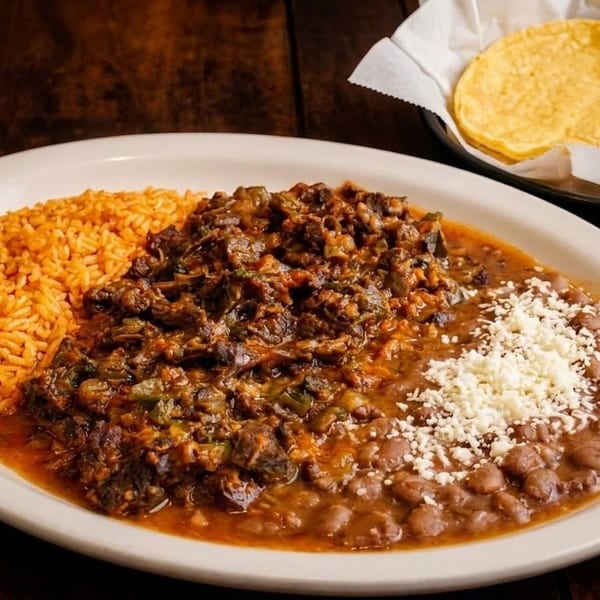 A plate of Mexican food with rice, stewed meat, beans with cheese, and a side of tortillas.