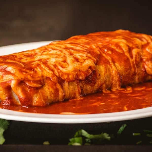 A large, saucy burrito covered in melted cheese and red sauce on a white plate.