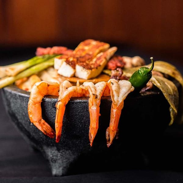 Molcajete filled with grilled shrimp, cheese, green onions, and a green chili.