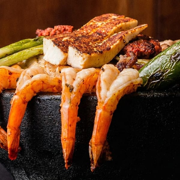 Grilled shrimp, cheese, green onions, and peppers served in a dark stone bowl.